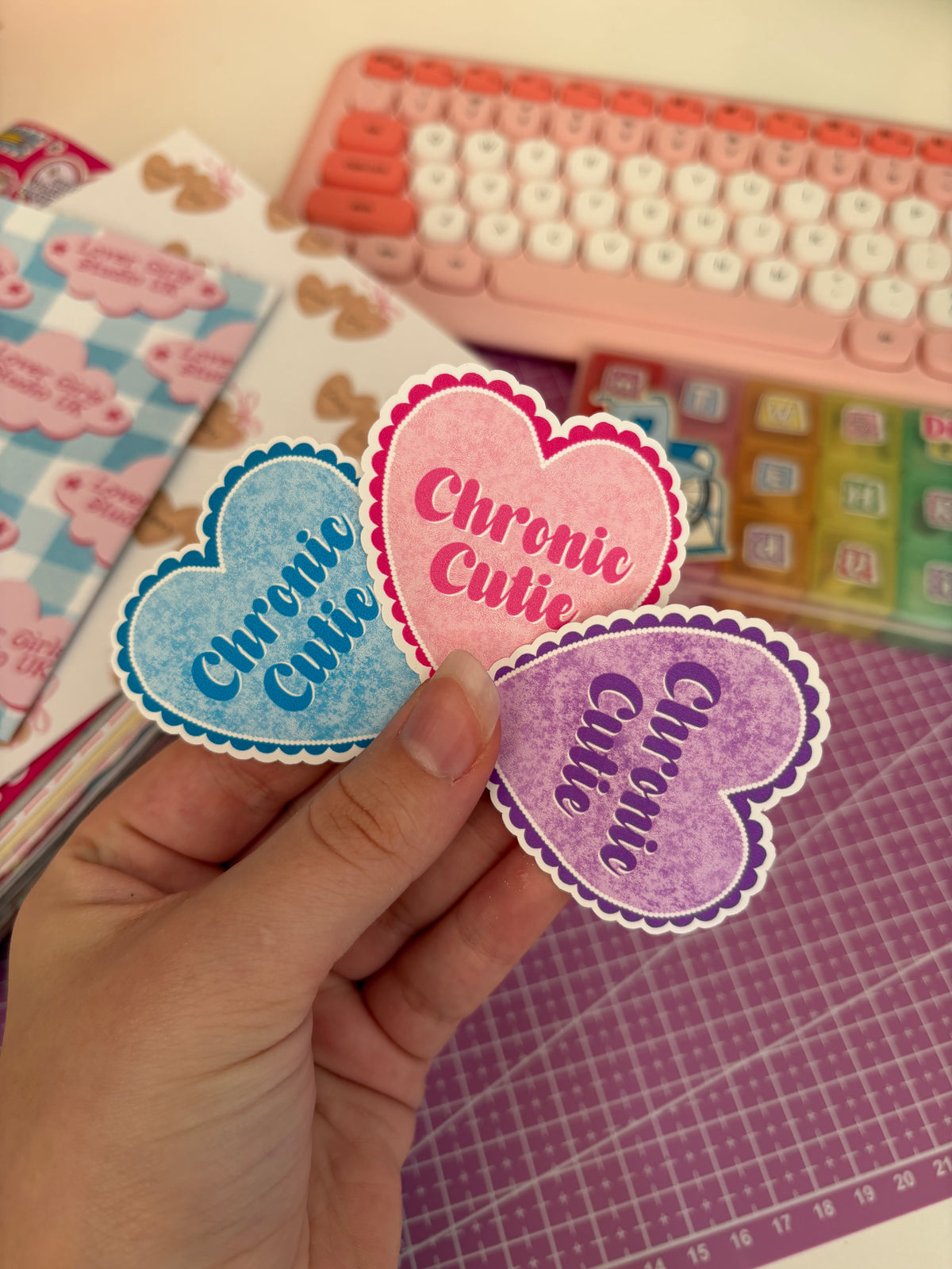 Three heart-shaped stickers in blue, pink, and purple are held up by a hand. Each sticker features the text 'Chronic Culi' in a stylized font with a scalloped border.